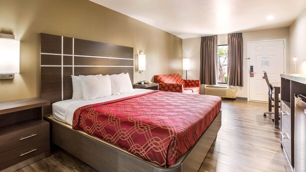 A hotel room with a large bed, a desk, a chair, and a desk lamp.