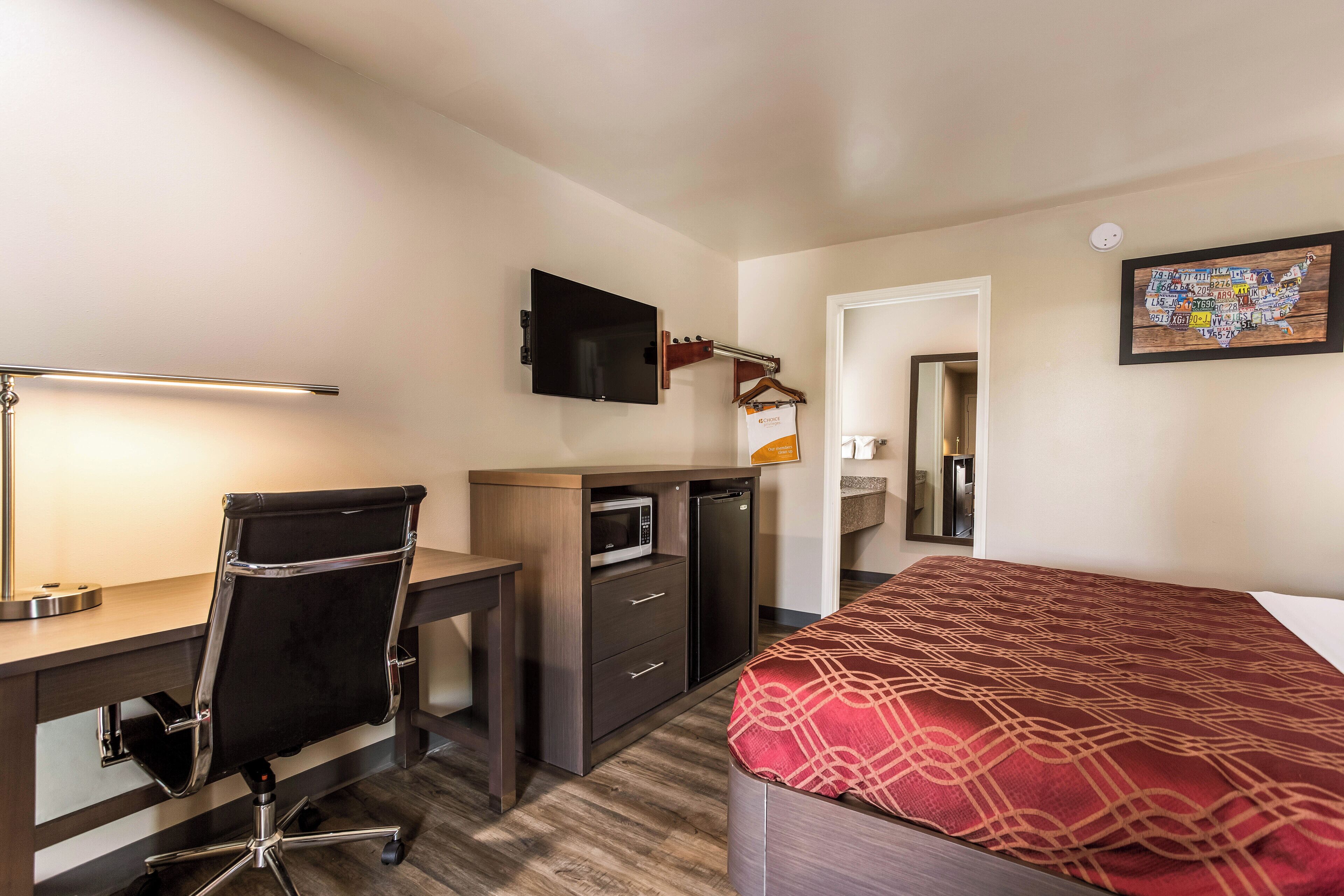 A hotel room with a desk, chair, bed, TV, and a microwave.
