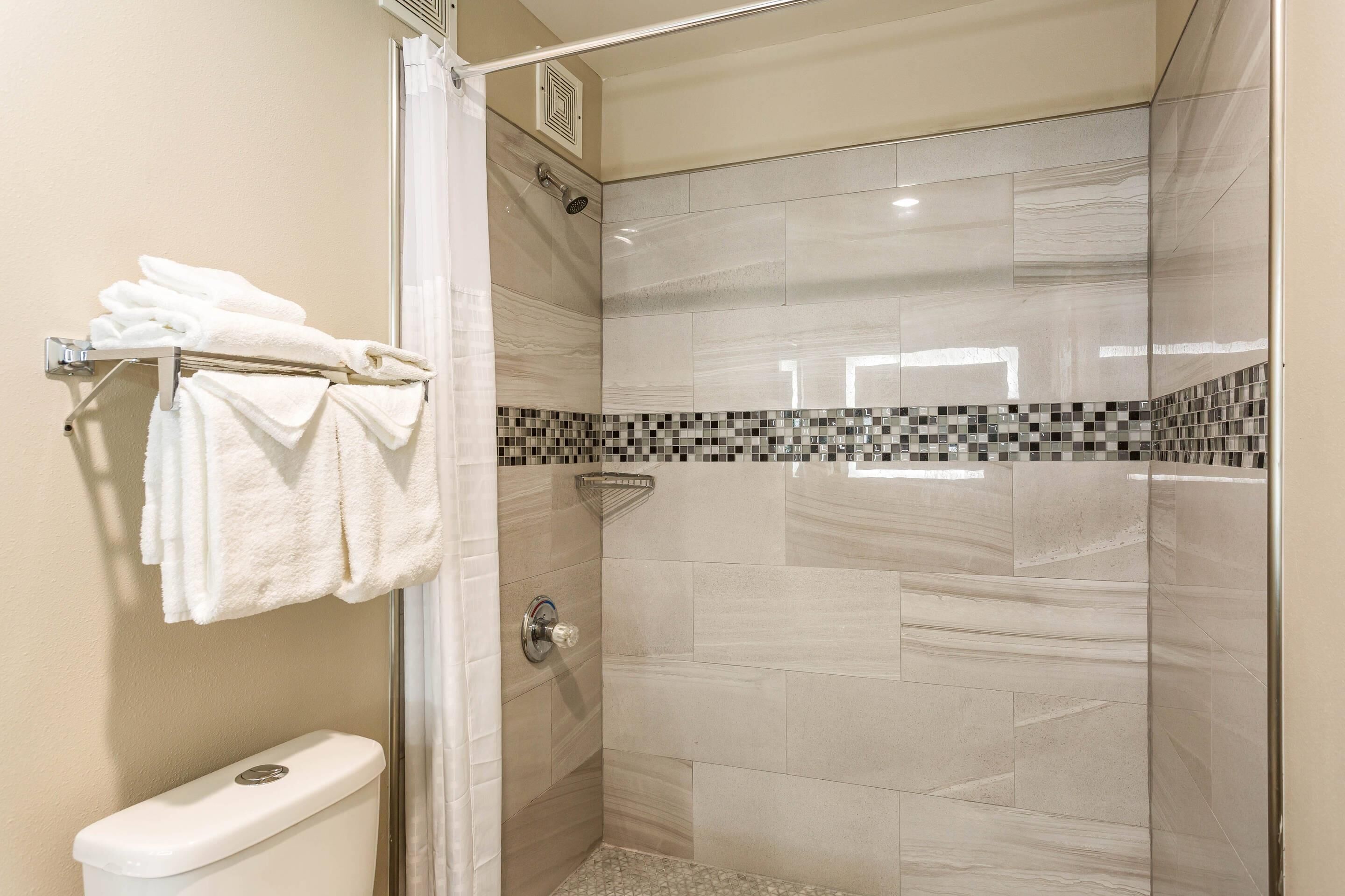 A shower with a glass door, a toilet, and a towel rack with folded towels.