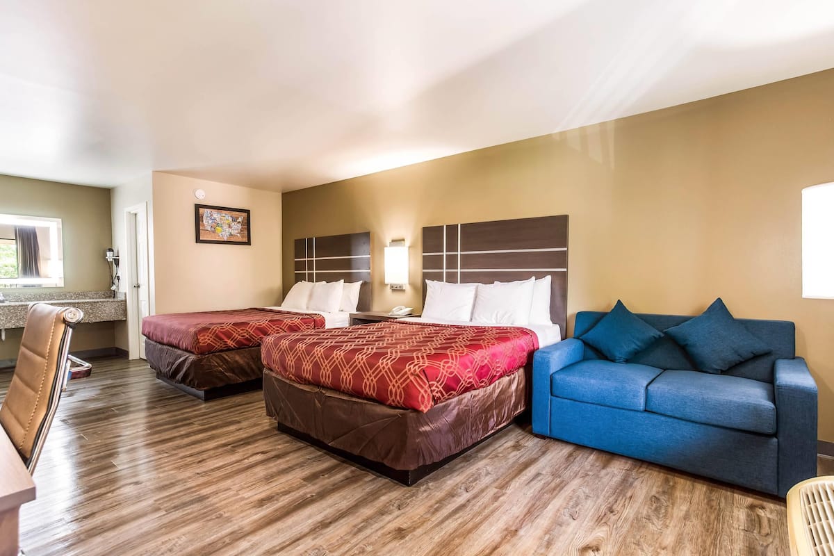 A hotel room with two beds, a blue sofa, a wooden floor, and a window with a view.