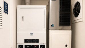 A compact laundry room with a front-loading washer, a stacked dryer, and a wall-mounted air conditioning unit.