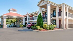 A multi-story motel with a central atrium, a red-roofed structure, and a parking area with cars.