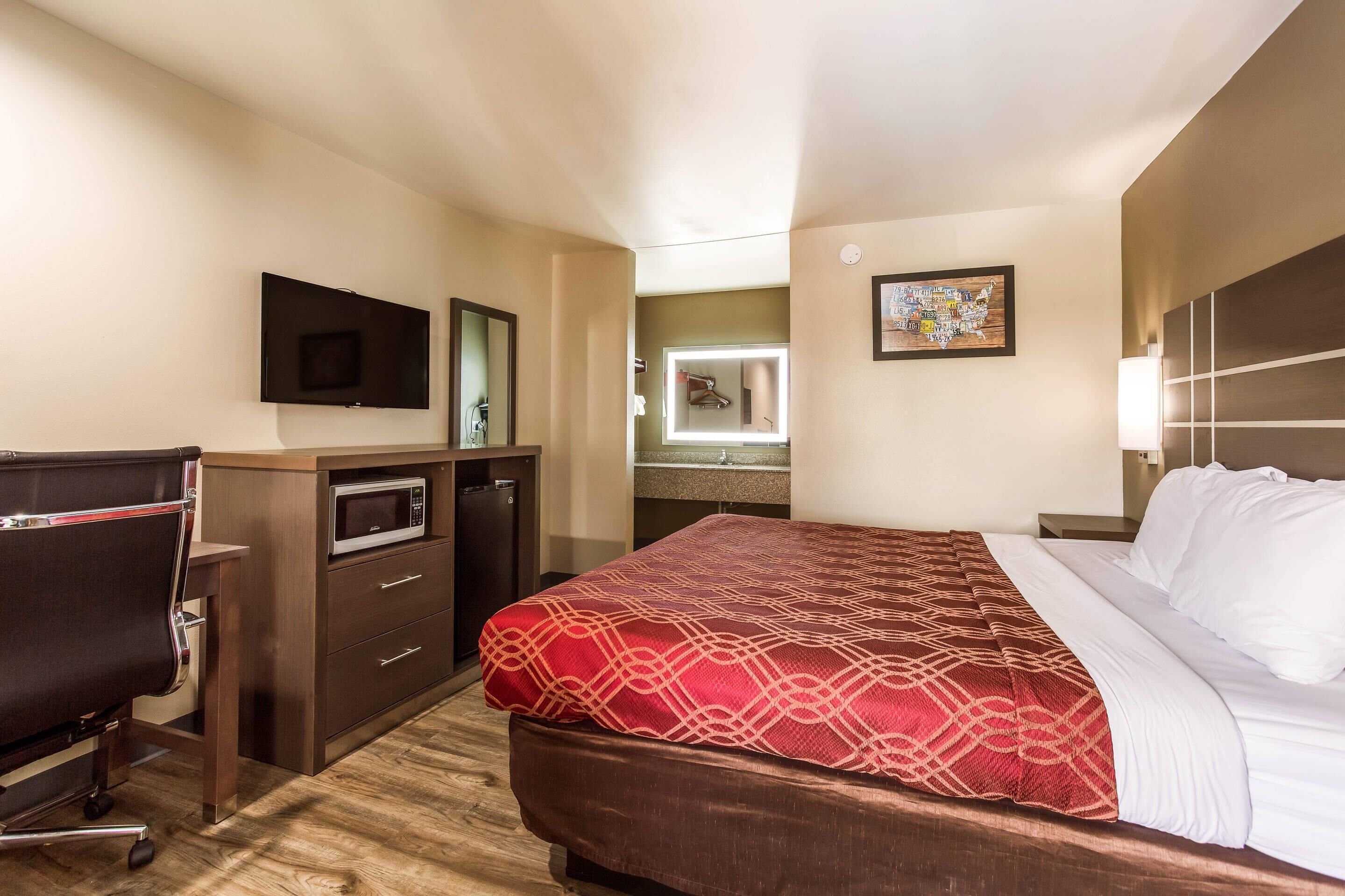 A hotel room with a bed, a desk, a TV, a microwave, and a bathroom visible through an open door.