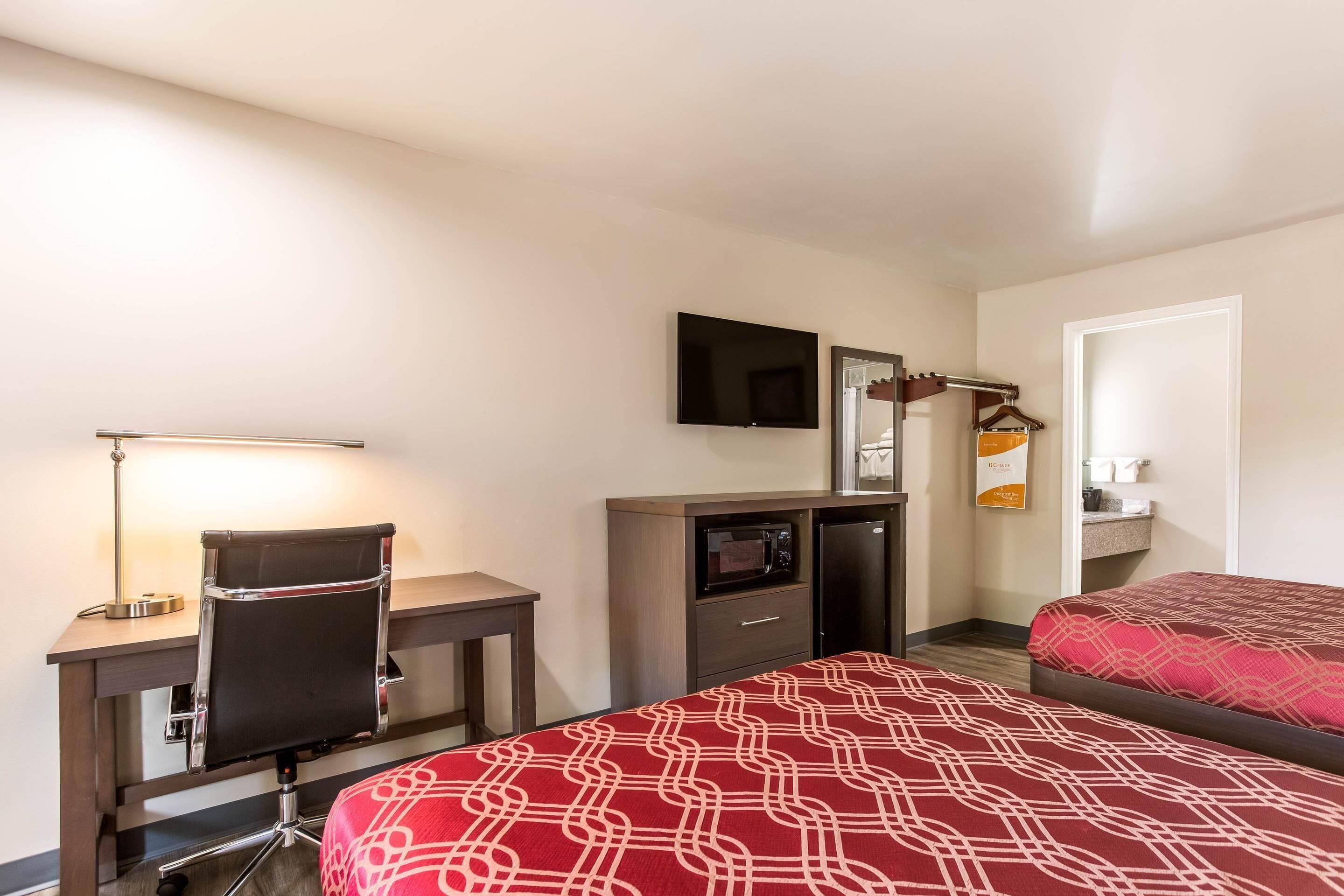 Une chambre d’hôtel équipée d’un bureau, d’une chaise, de deux lits, d’une télévision, d’un four à micro-ondes et d’un petit placard.