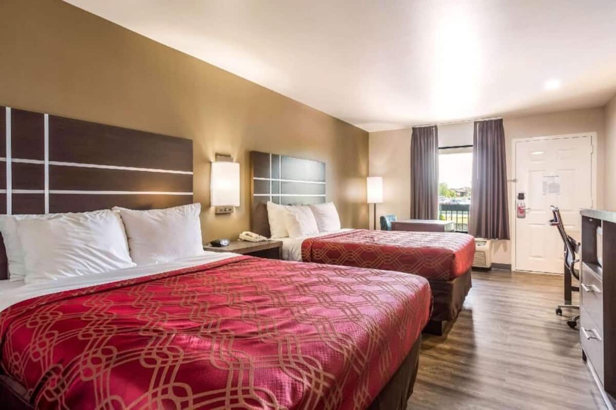 A hotel room with two beds, a desk, a chair, a wardrobe, and a window with curtains.