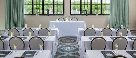 A conference room with tables set for a meeting, large windows with a view of greenery, and a patterned carpet.