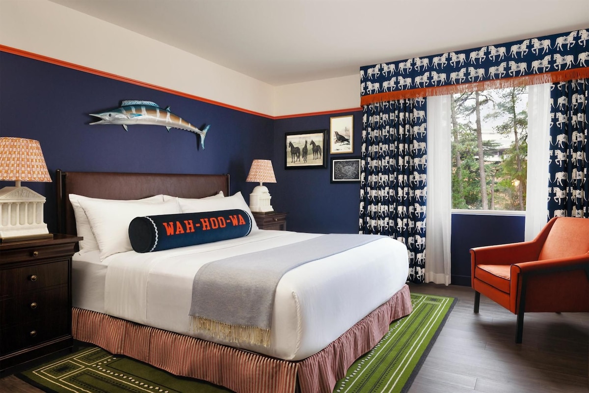 A hotel room with a large bed, a nightstand, a lamp, a chair, and a window with curtains.