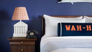 A hotel room with a bed, a nightstand with a lamp, a telephone, a decorative pillow, and a wall decoration.