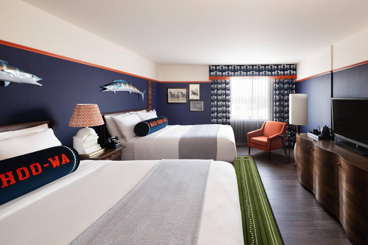 A hotel room with two beds, a TV, a desk, and a chair.