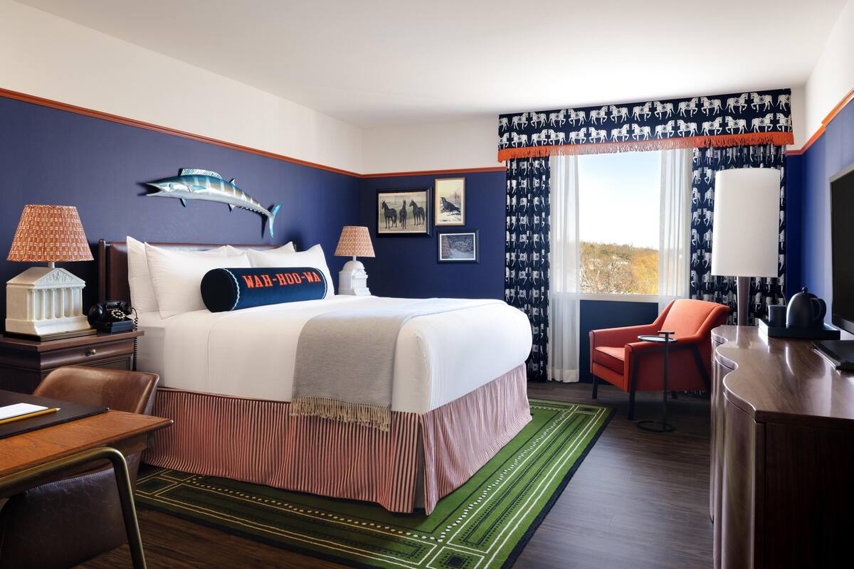 A hotel room with a large bed, two bedside tables with lamps, a desk, a chair, and a view of the outdoors.