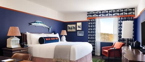 A hotel room with a large bed, two bedside tables with lamps, a desk, a chair, and a view of the outdoors.