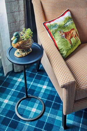 A checkered sofa with a cushion featuring a landscape scene, a small round table with a decorative item, and a blue checkered floor.