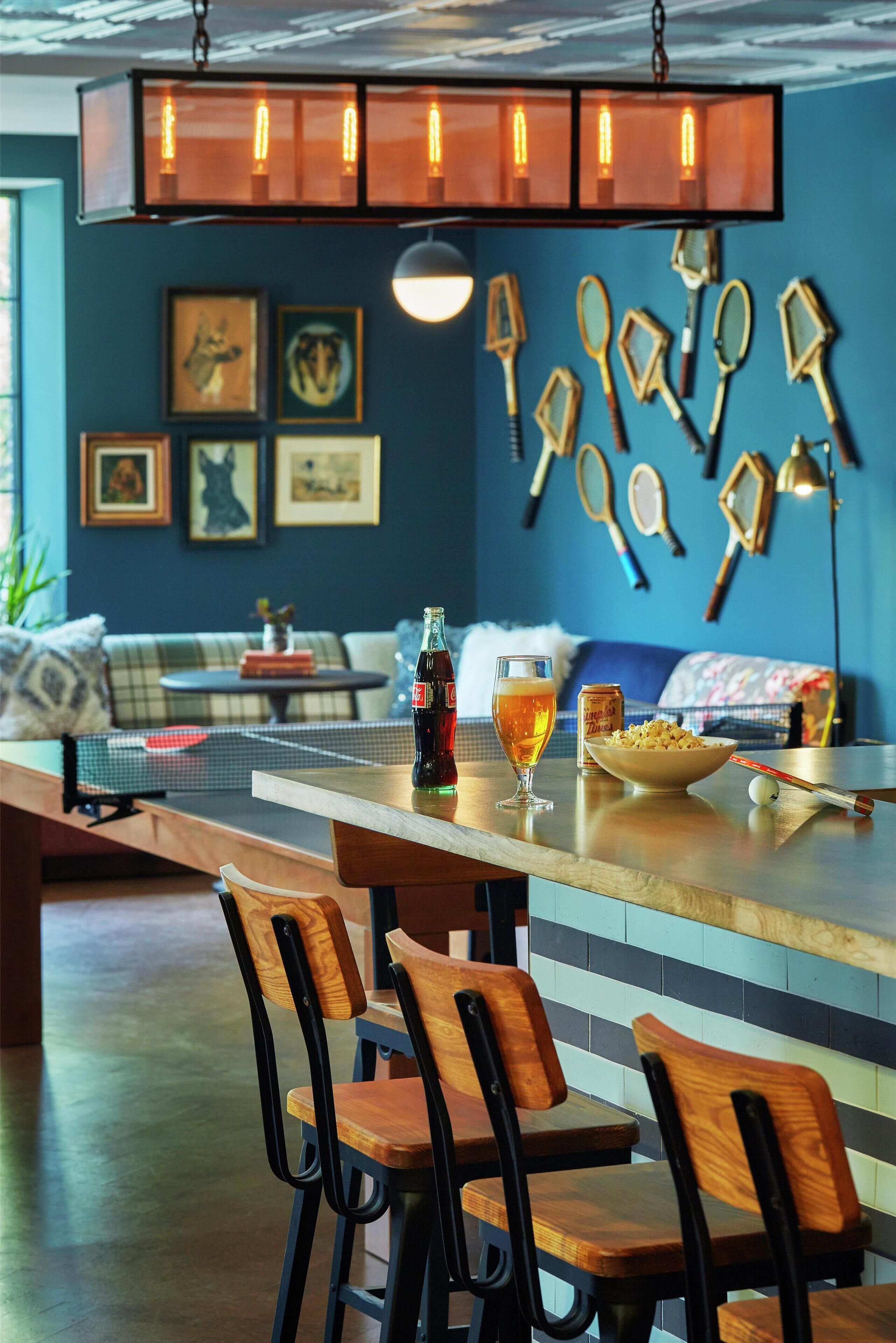 A bar area with wooden chairs, a table with a bottle of soda, a bowl of popcorn, and a ping pong table.