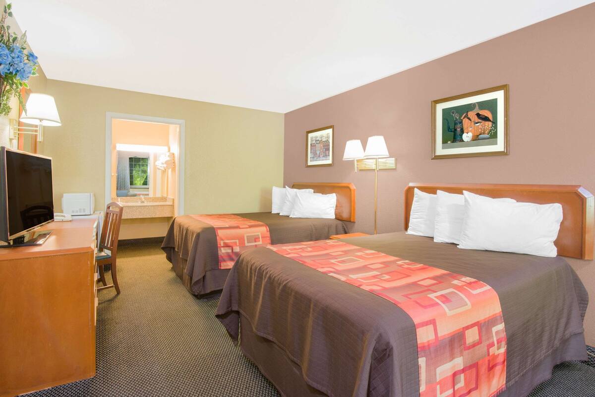 Een hotelkamer met twee bedden, een bureau met een televisie, een stoel en een raam.