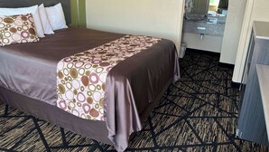 Une chambre d’hôtel avec un grand lit, une table de chevet, un miroir et une salle de bain visible à travers une porte ouverte.