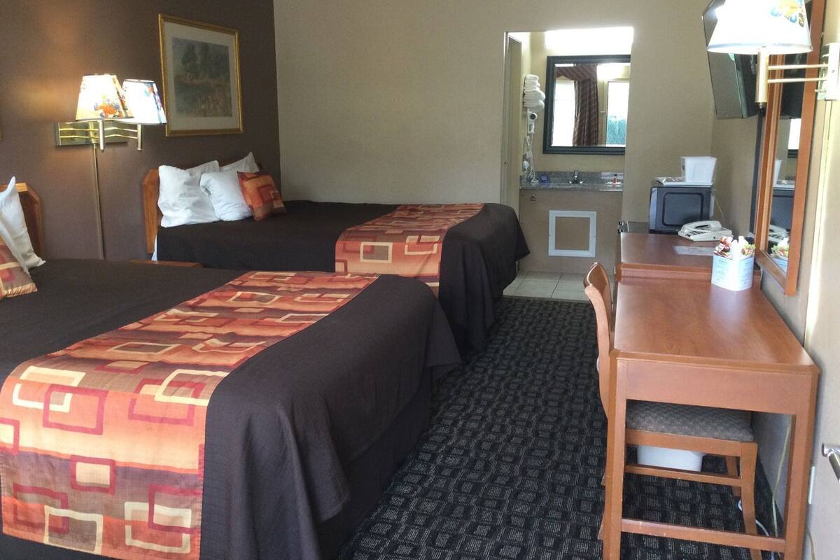 Een hotelkamer met twee bedden, een bureau, een stoel, een spiegel, een kleine kitchenette en een lijst aan de muur.