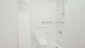 Un baño blanco con ducha, inodoro y barra de apoyo.