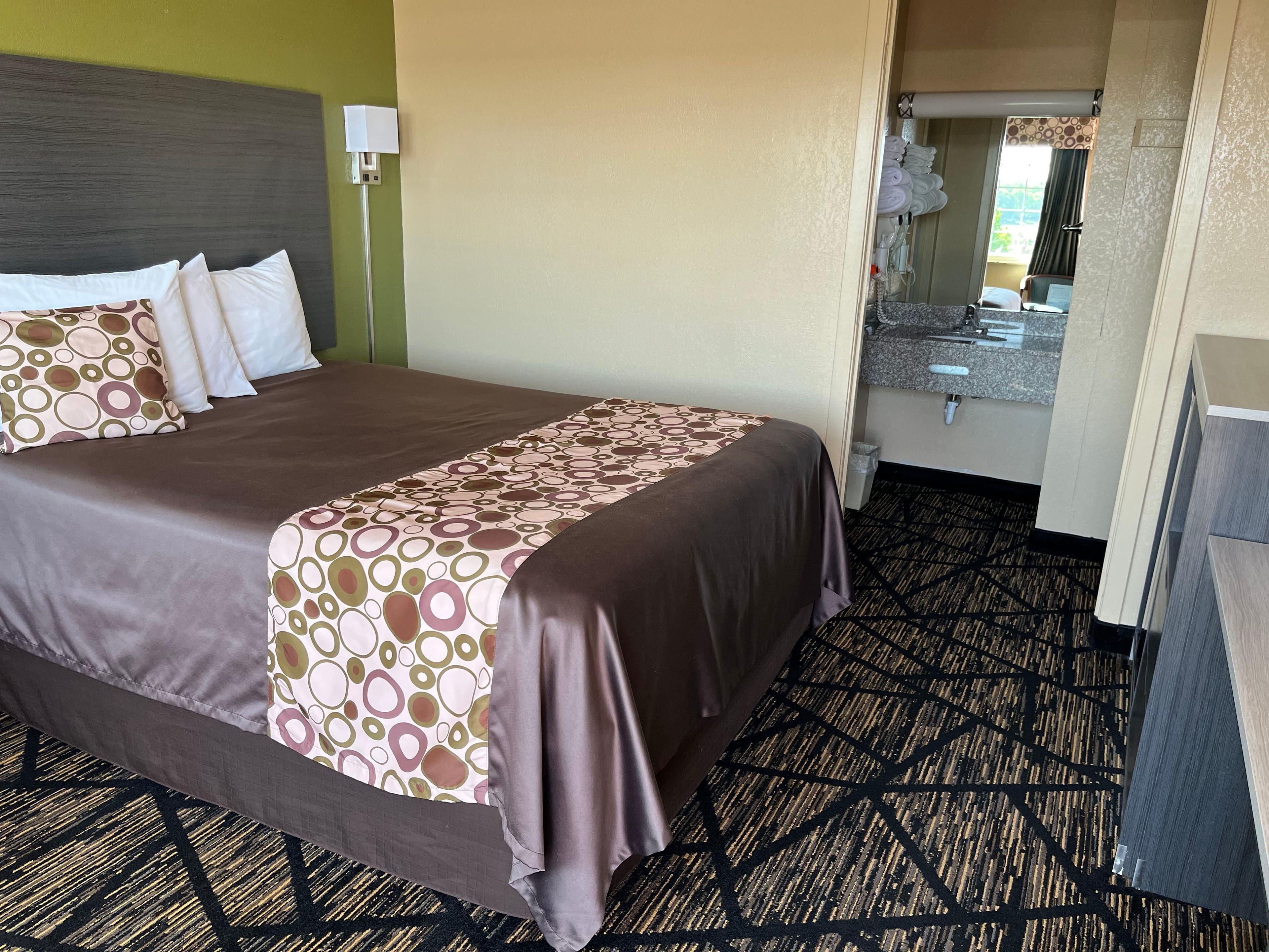 A hotel room with a large bed, a bedside table, a mirror, and a bathroom visible through an open door.