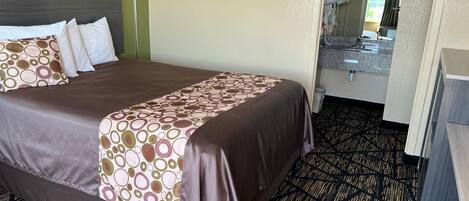 A hotel room with a large bed, a bedside table, a mirror, and a bathroom visible through an open door.