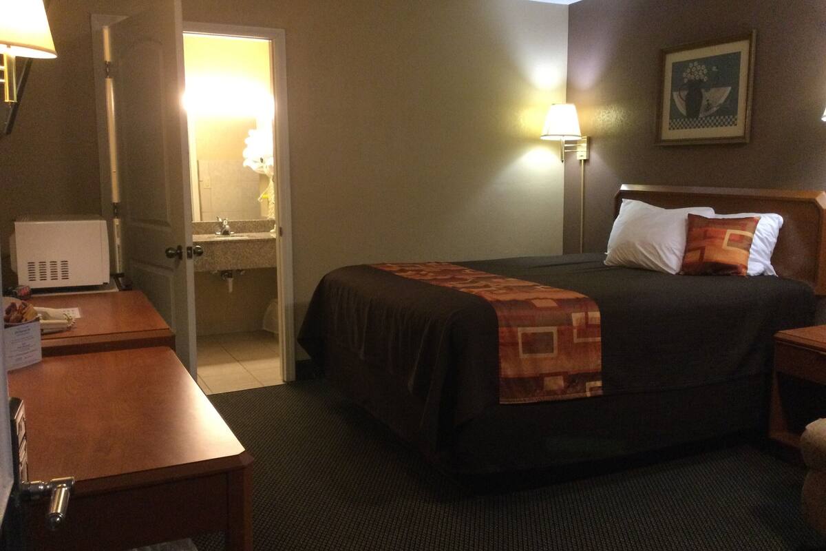 Een hotelkamer met een bed, nachtkastje, lamp en een deur naar de badkamer.