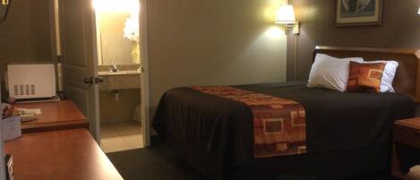 A hotel room with a bed, bedside table, lamp, and a door leading to a bathroom.