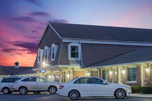 Un hôtel à la façade en briques, doté de nombreuses fenêtres et d’une enseigne indiquant qu’il s’agit d’un immeuble de bureaux. Deux voitures sont garées devant.