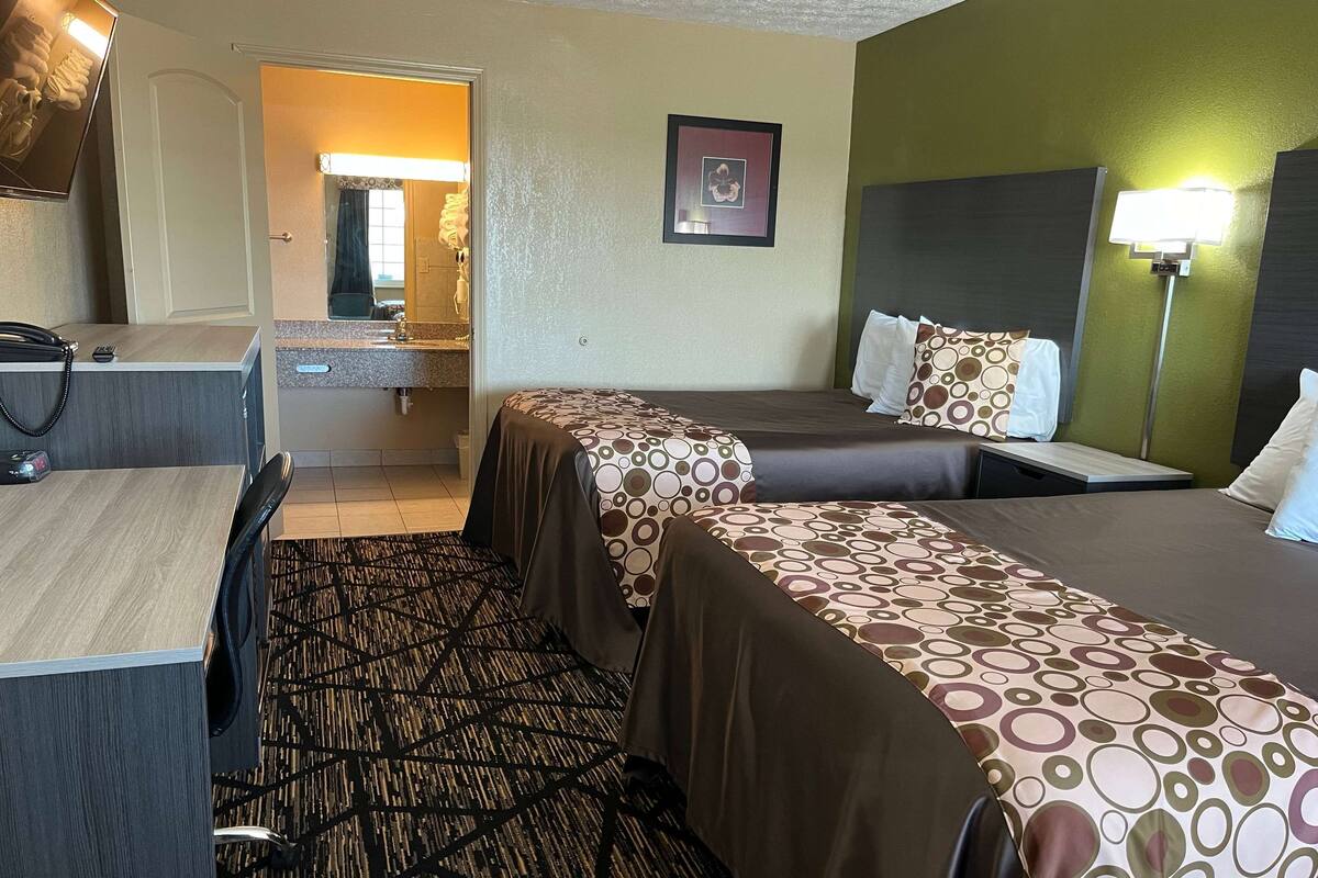Hotelkamer met twee bedden, een bureau, een stoel, een badkamer met spiegel en een nachtkastje.
