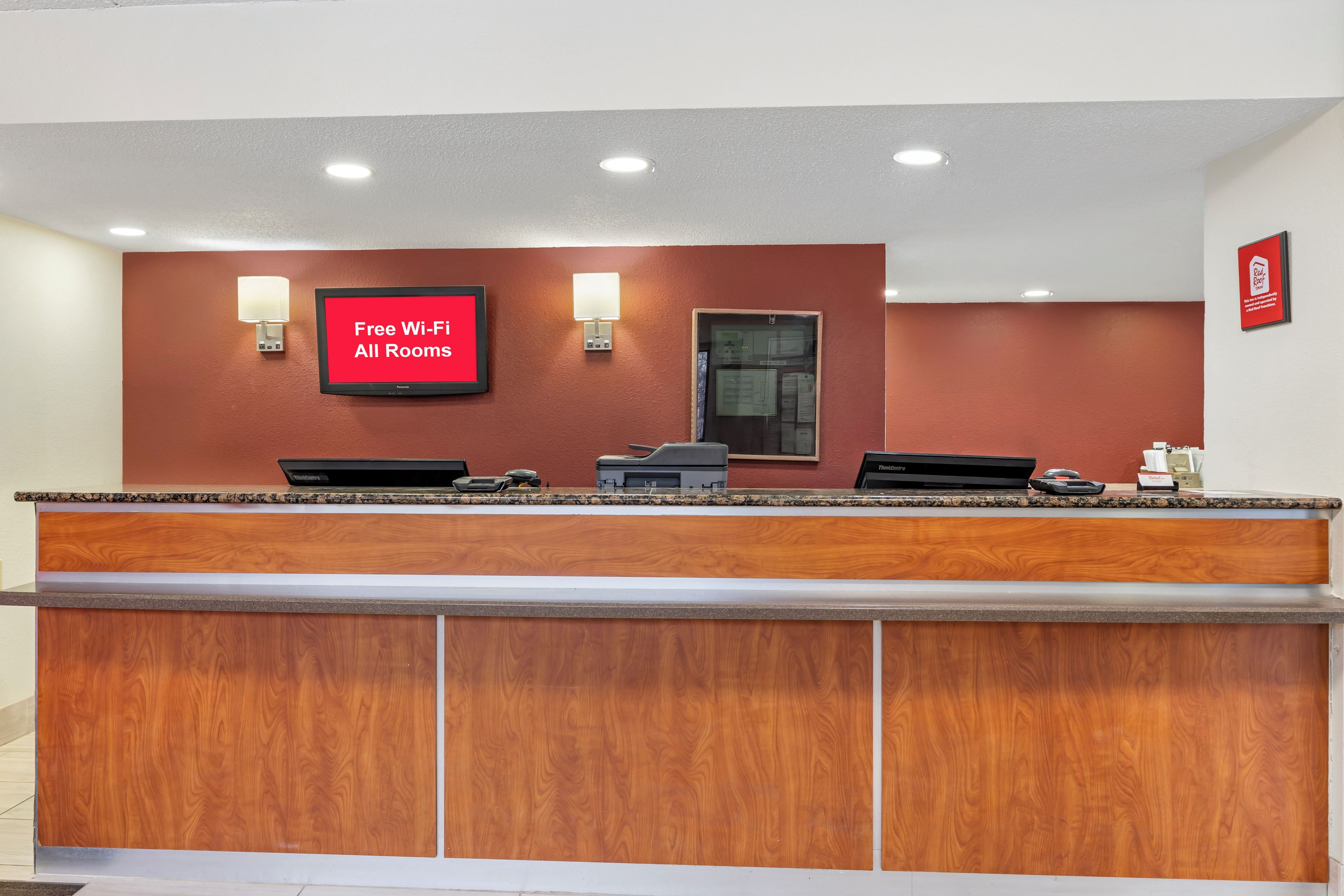 Balcão de recepção de hotel com uma TV de tela plana exibindo 'Wi-Fi Grátis em Todos os Quartos' e a placa da Red Roof Inn.