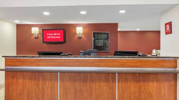 Balcão de recepção de hotel com uma TV de tela plana exibindo 'Wi-Fi Grátis em Todos os Quartos' e a placa da Red Roof Inn.
