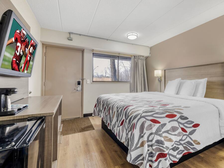 Una camera d'albergo con un letto, una scrivania, una macchina del caffè, una finestra con tende e una TV a parete.