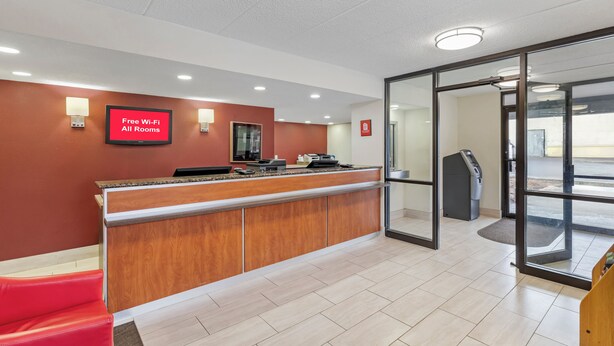 A reception area with a red wall, a digital screen advertising free Wi-Fi, a reception desk, and a glass door leading outside. - Red Roof Inn Parsippany (Parsippany)