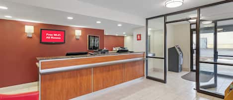 A reception area with a red wall, a digital screen advertising free Wi-Fi, a reception desk, and a glass door leading outside.