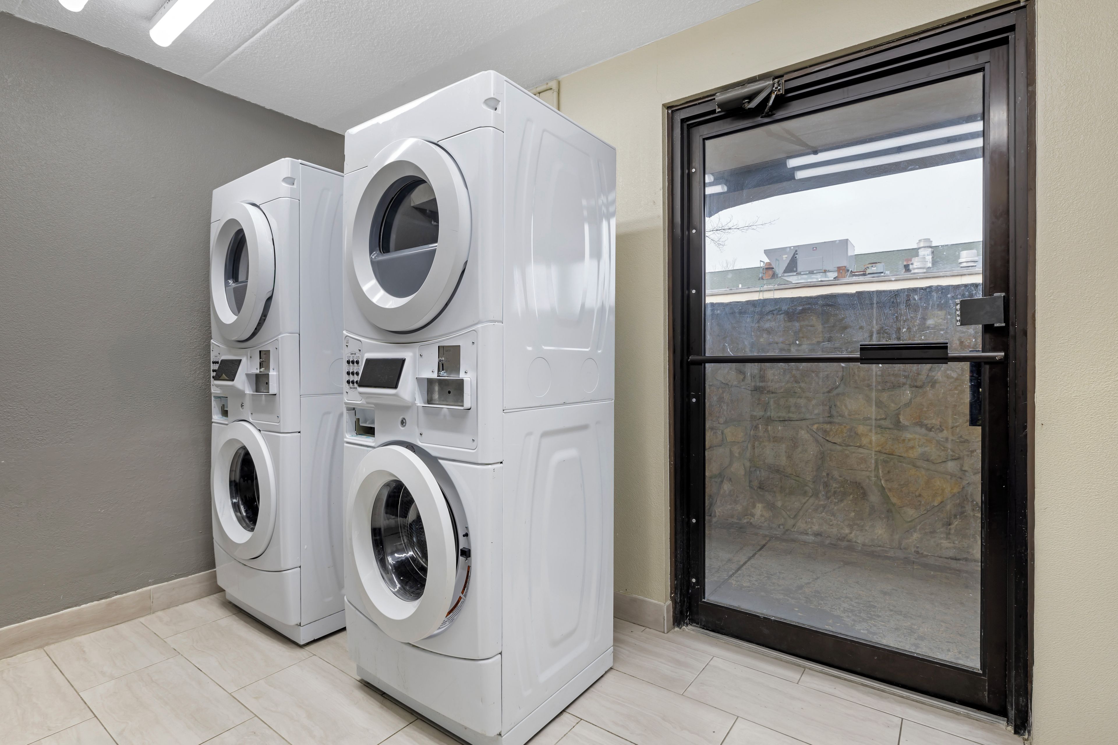 A laundry room with two stacked front-loading washing machines and a glass door leading outside.