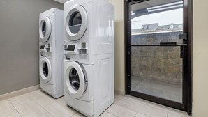 A laundry room with two stacked front-loading washing machines and a glass door leading outside. - Red Roof Inn Parsippany (Parsippany)