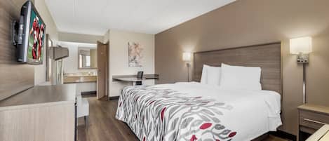 A hotel room with a bed, bedside tables, a desk, a chair, a flat-screen TV, and a painting on the wall.