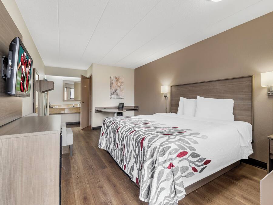 A hotel room with a bed, bedside tables, a desk, a chair, a flat-screen TV, and a painting on the wall.