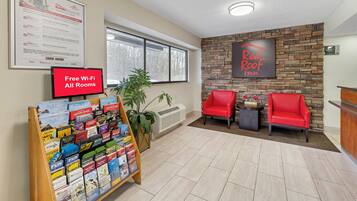 A Red Roof Inn reception area with a Red Roof Rewards program poster, a Red Roof Plus sign, a Red Roof mobile app download sign, a Red Roof Inn sign, a Red Roof logo, and a Red Roof Inn sign with a 4-star rating.