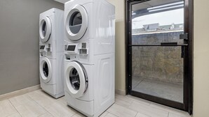 A laundry room with two stacked front-loading washing machines and a glass door leading outside. - Red Roof Inn Parsippany (Parsippany)