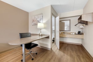 A hotel room with a wooden floor, a dining table with a chair, a lamp, a bathroom visible through an open door, and a kitchen area with a countertop and hanging towel. - Red Roof Inn Parsippany (Parsippany)