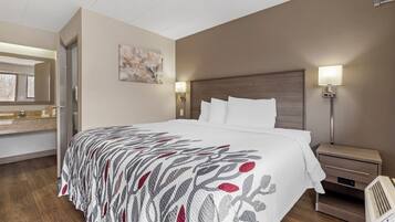 Una habitación de hotel con cama, mesitas de noche, lámpara, espejo y una obra de arte colgada en la pared.
