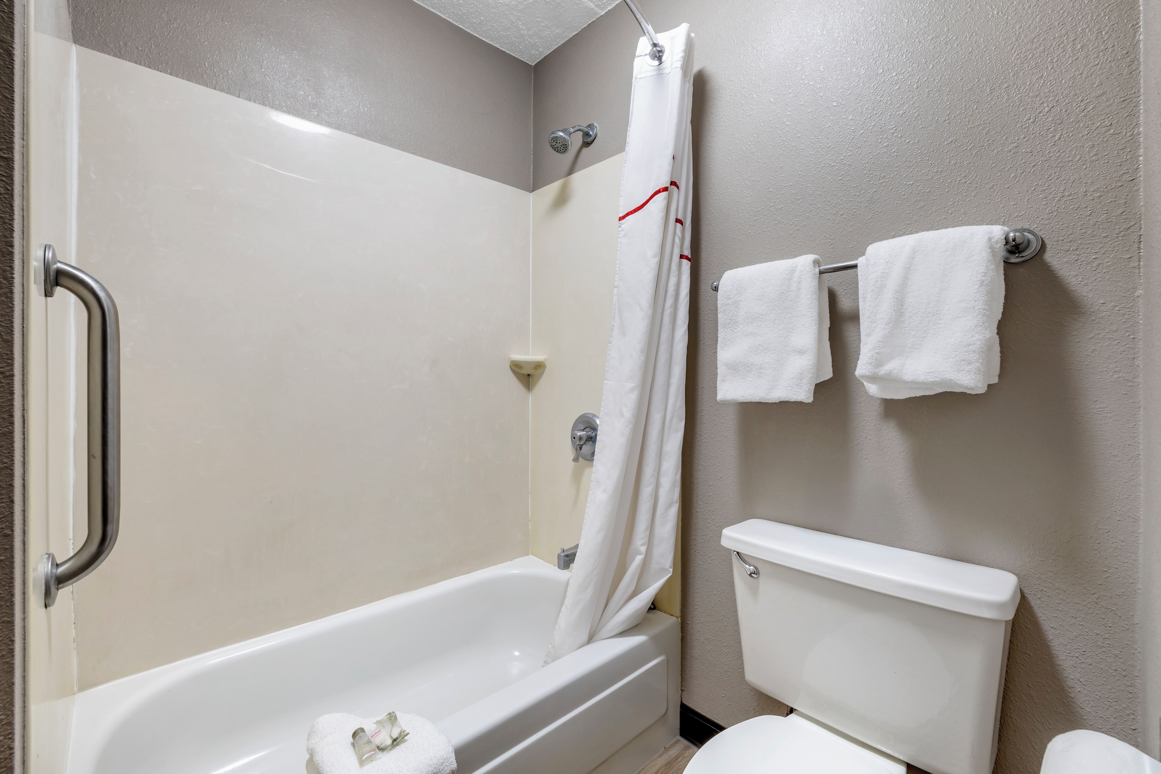 A bathroom with a bathtub, shower, toilet, and a towel rack with two towels.