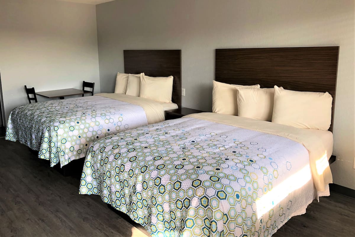 Habitación de hotel con dos camas, cada una con cabecero, una mesita y dos sillas.