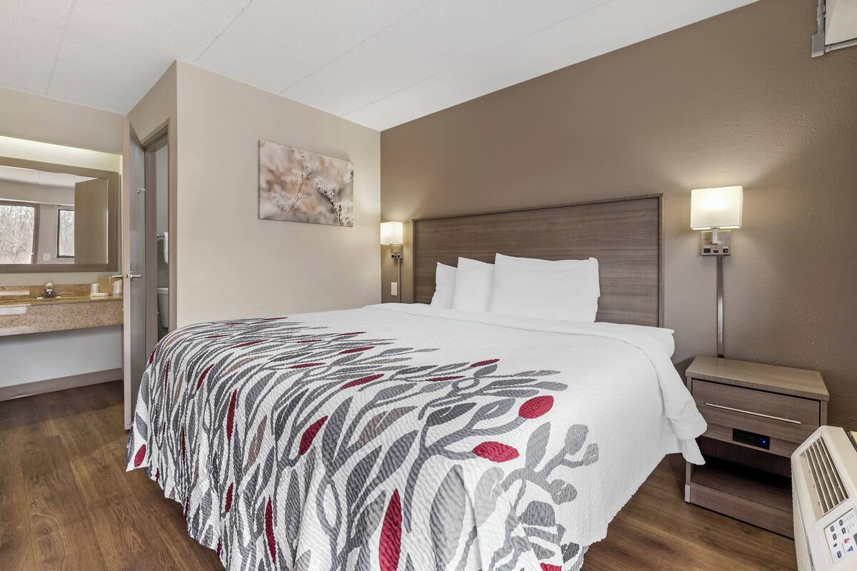 Ett hotellrum med en säng, ett nattduksbord, en lampa, en spegel och en tavla på väggen.
