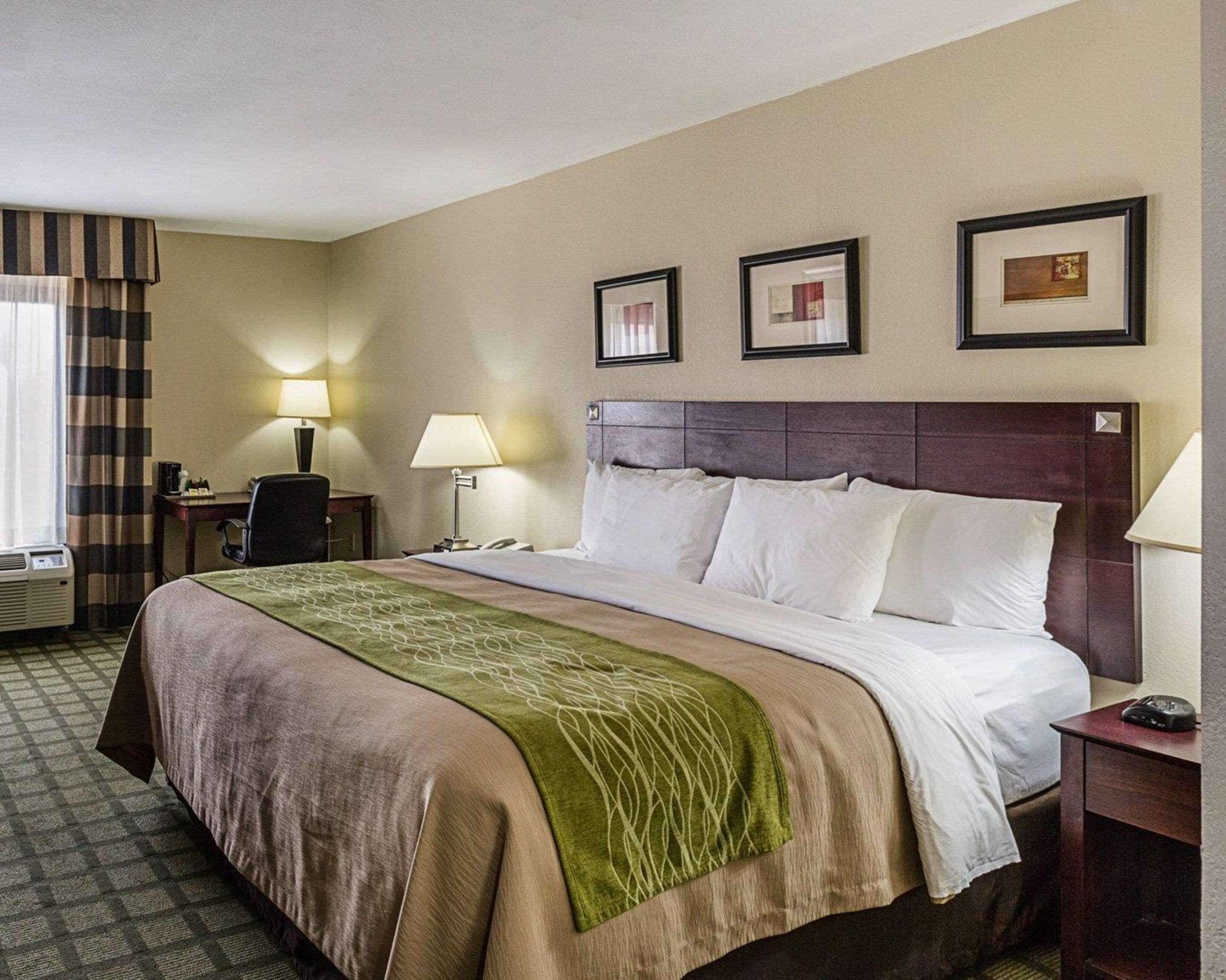 A hotel room with a large bed, two bedside tables, a desk, and a chair. There are three framed pictures on the wall.