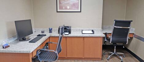 A hotel room with a desk, computer, and two office chairs.