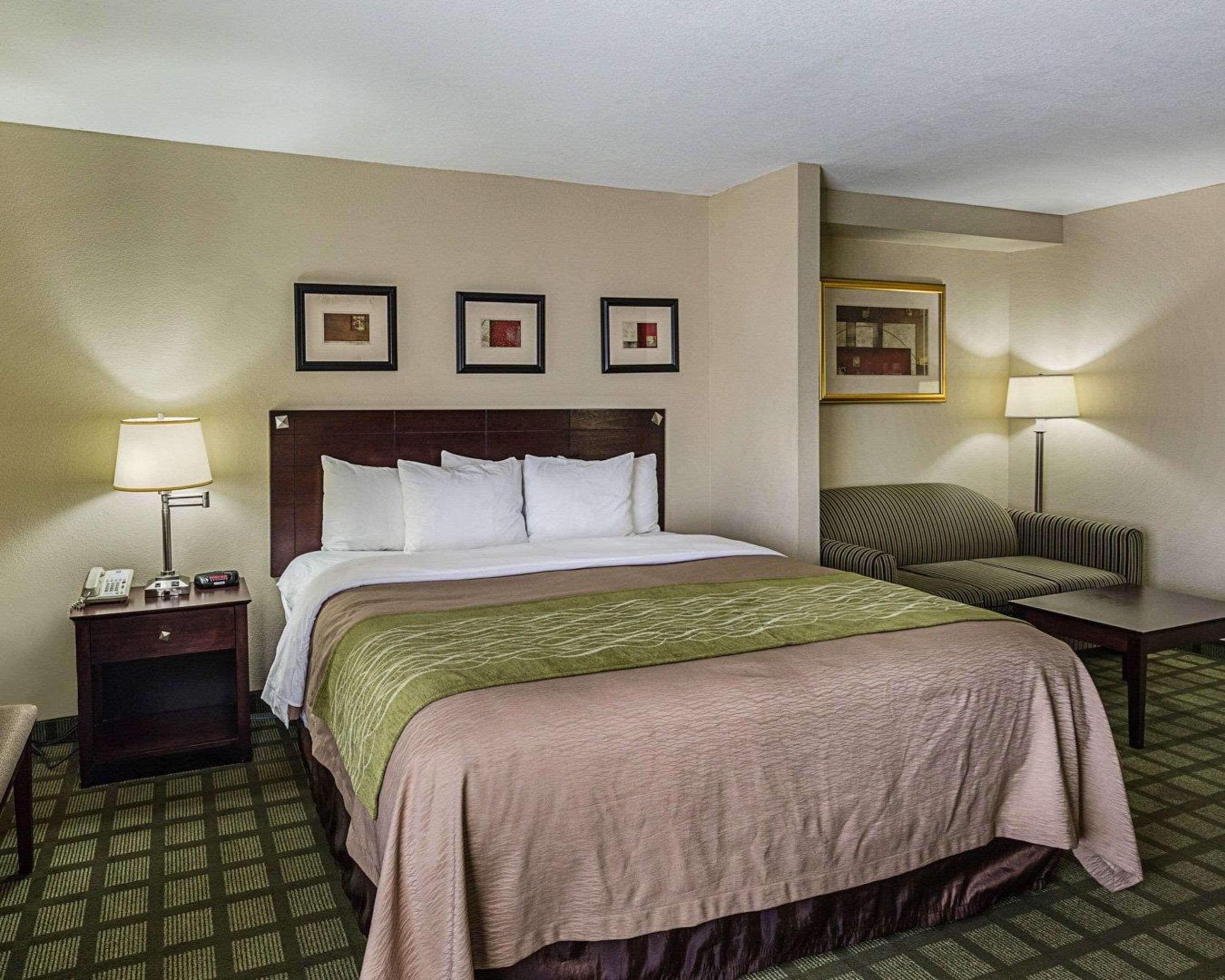 A hotel room with a bed, a nightstand with a lamp, a chair, and a small table.