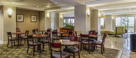 Un hall d’hôtel doté de plusieurs espaces de détente, notamment des tables et des chaises rondes, un comptoir d’accueil et une grande fenêtre offrant une vue sur l’extérieur.