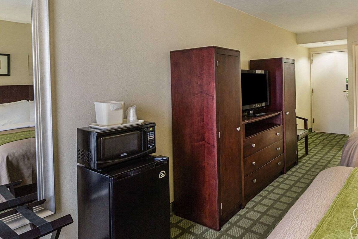 Une chambre d’hôtel équipée d’un lit, d’un bureau avec un ordinateur, d’un micro-ondes, d’une télévision et d’une armoire.