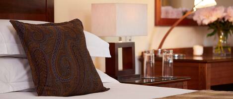 Habitación de hotel con cama bien hecha, una lámpara de noche, un jarrón con flores y una mesita de noche de madera.