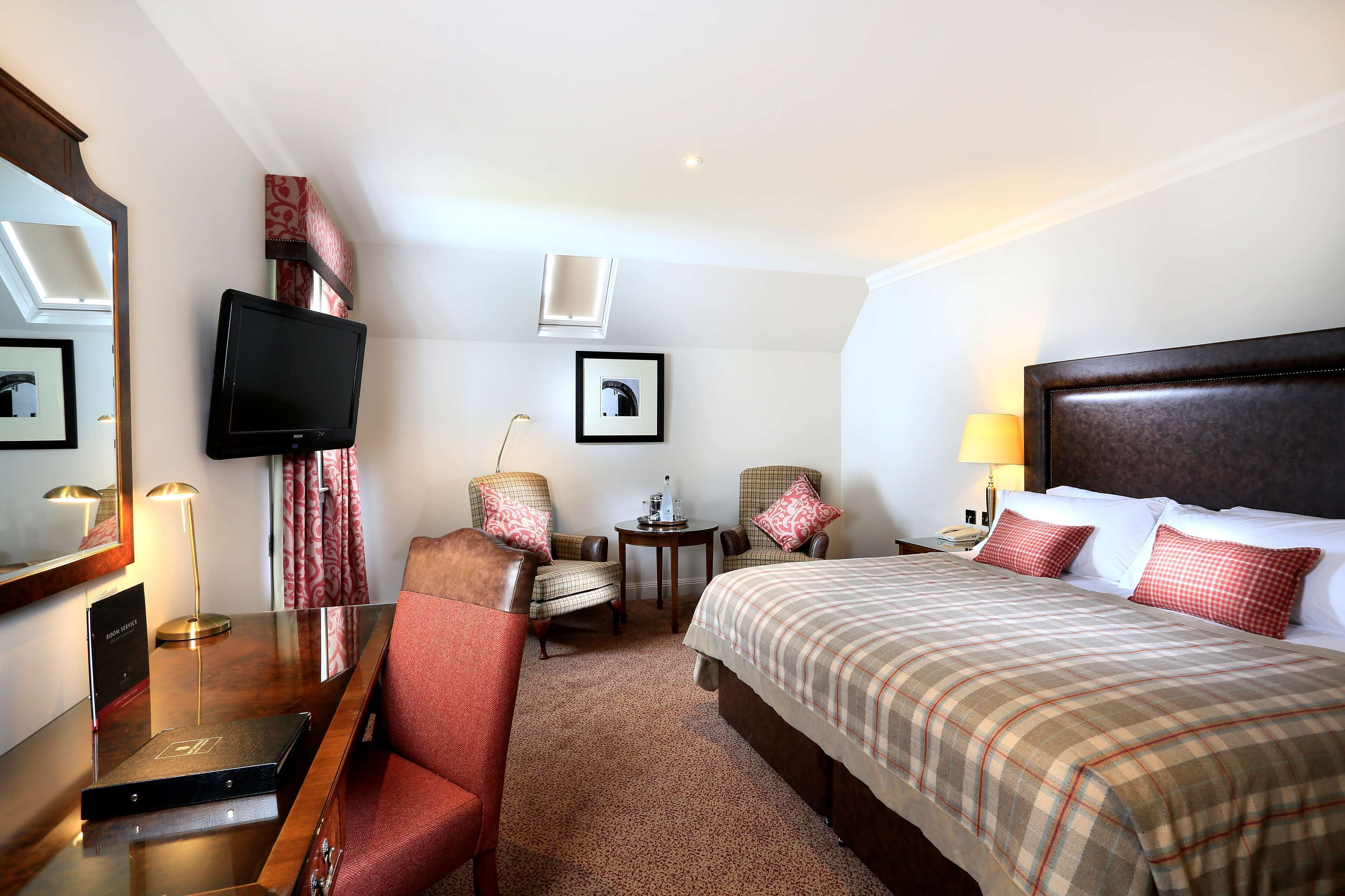 Ein Hotelzimmer mit einem Bett, zwei Sesseln, einem Schreibtisch mit Fernseher, einem kleinen Tisch und einer Lampe.